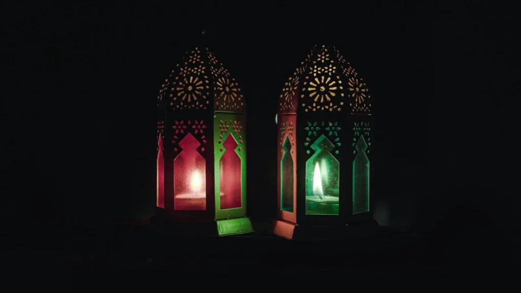 Two lit lanterns with Islamic patterns glowing in the dark
