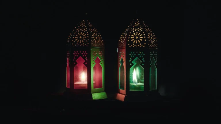 Two lit lanterns with Islamic patterns glowing in the dark