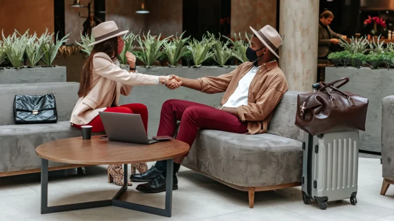Two travellers shaking hands in a lounge with their luggage beside them