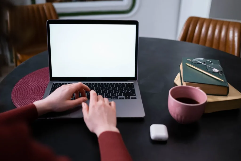 Hands typing on a laptop at a home desk beside a coffee cup and books