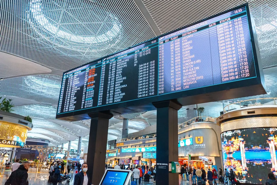 Passengers walking through an airport departures area with shops and flight screens