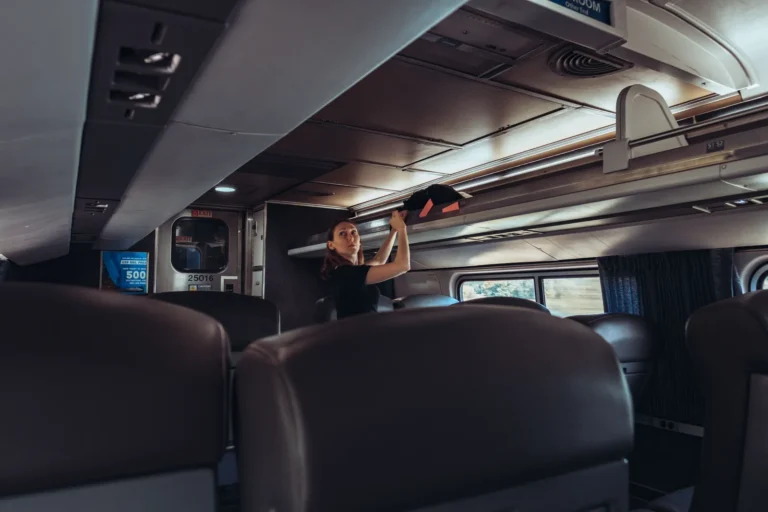 A traveller placing a bag on an overhead luggage rack inside a train carriage